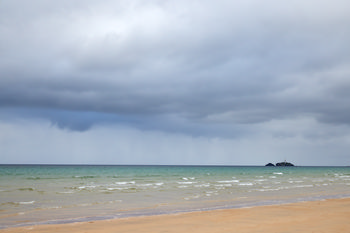 Godrevy beach colours This landscape photograph depicts Godrevy beach in Cornwall, England, during the early evening in summer. The scene highlights the natural colours of the beach under a cloudy sky, with gentle waves washing onto the sandy shore and the turquoise sea stretching out towards the horizon. To the right, the image features Godrevy Island with its recognisable lighthouse, a notable landmark on this part of the Cornish coast. The overall atmosphere is characteristic of the United Kingdom’s coastal scenery, with muted tones and a wide expanse of open water typical of a summer evening by the sea.